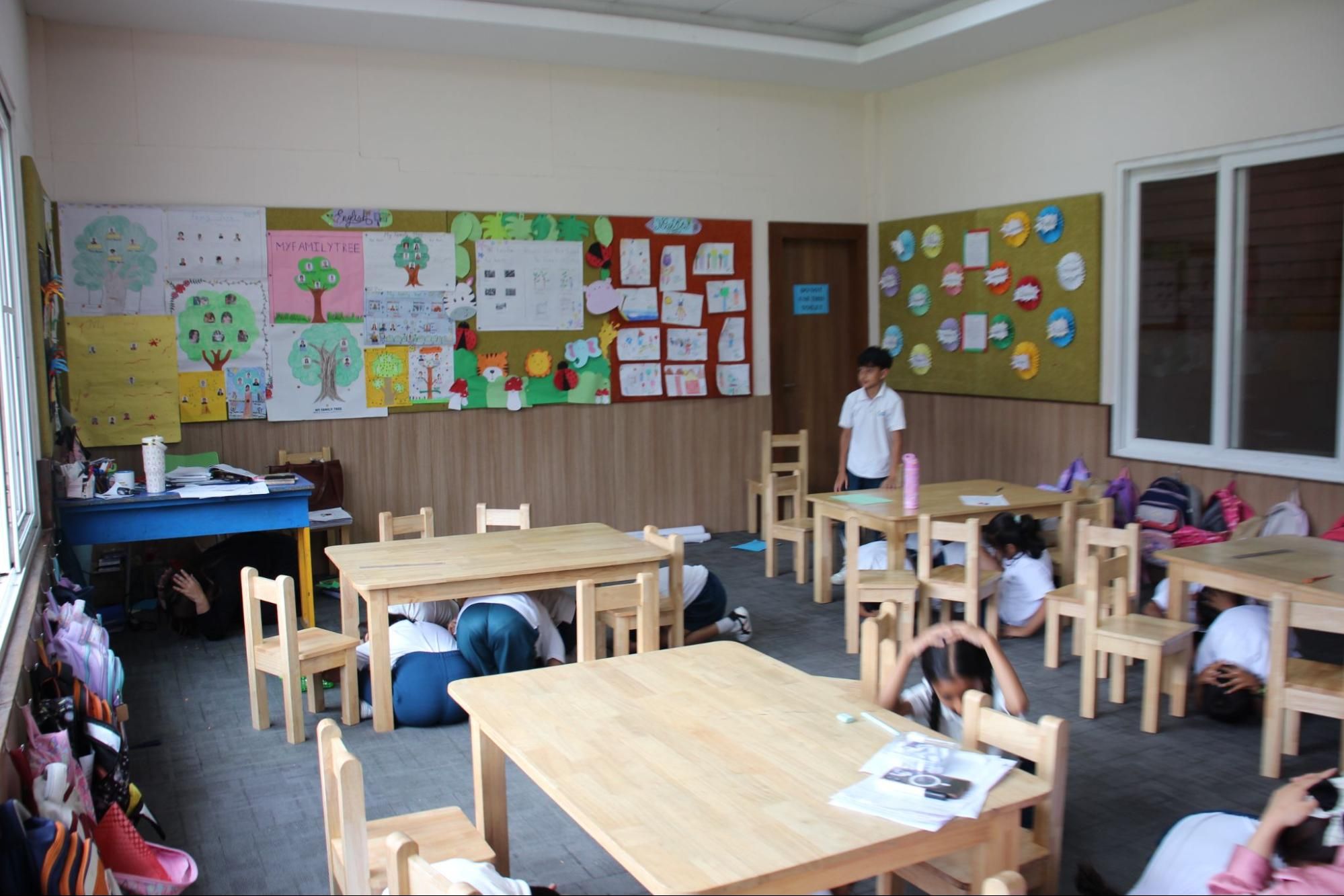 Imperial World School students practice earthquake safety measures under classroom tables during a disaster preparedness exercise.