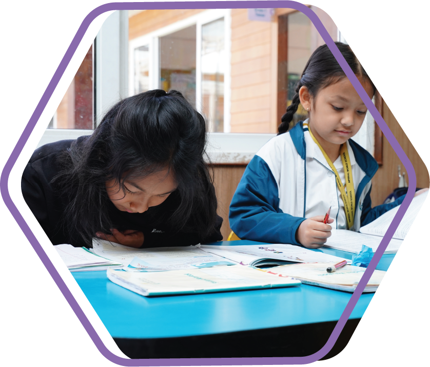 Two young girls focused on writing in their notebooks during a classroom activity.