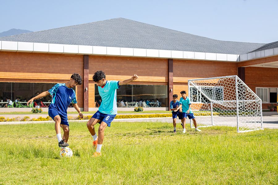 Students at Imperial World School playing soccer on a grassy field, engaging in outdoor sports activities.
