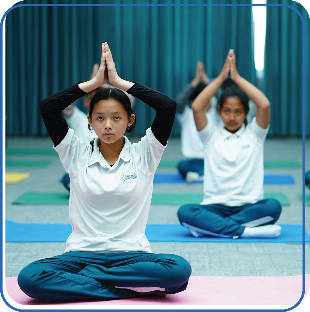 Students at Imperial World School practicing yoga during an extracurricular activity, sitting cross-legged on mats in a gym.